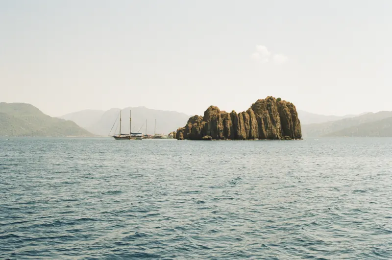A rocky island and sailboats against hazy mountains